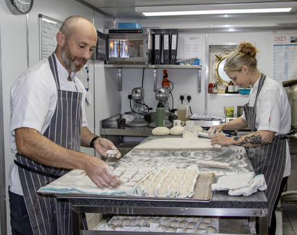 Two Chefs place bread roll dough on oven trays in the onboard Galley. 