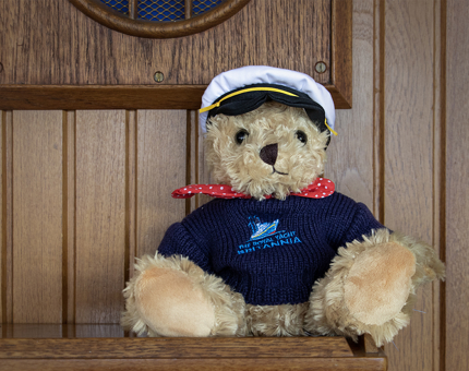 A teddy bear wearing a Britannia logo blue knitted jumper, red spotted necktie and Captain's hat. 