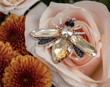 A topaz and crystal costume jewellery bee brooch. There are pink and orange flowers in the background. 