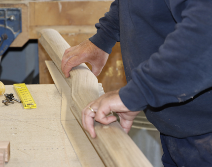 A Maintenance Team member holds a wooden handrail as he measures it up.