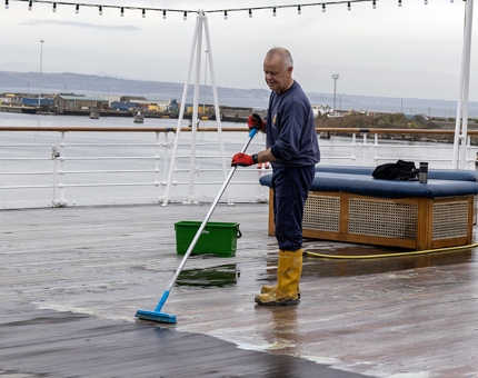 A man from the Maintenance team scrubbing the Verandah Deck with a broom.
