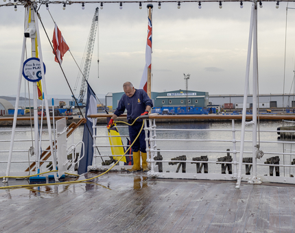 The Maintenance team member hosing down the wooden deck after scrubbing with a broom.