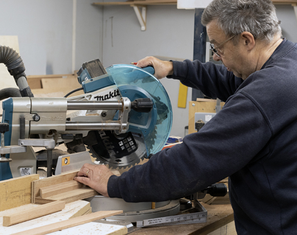 A Maintenance man uses a machine in the workshop to cut wooden edges for a display lectern.