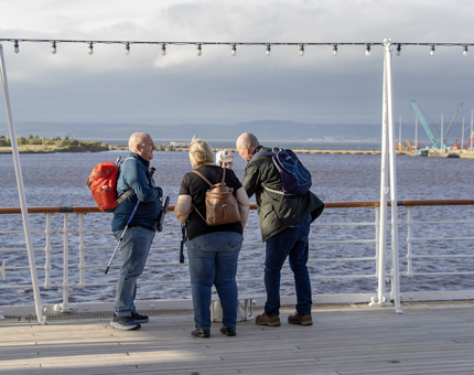 Two men and a woman look through a telescope onboard at the Verandah Deck.