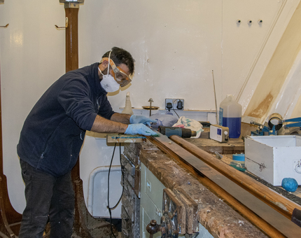 A man applying a rub to remove water marks from wooden handrails in a workshop.