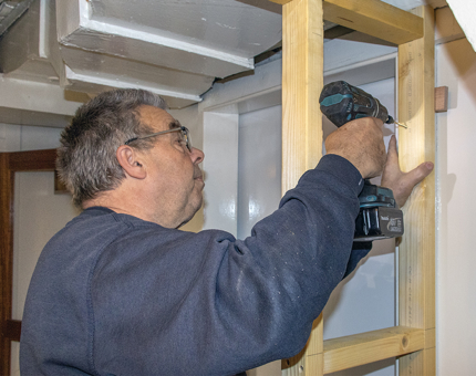 A man from the Maintenance team drilling into a doorframe.