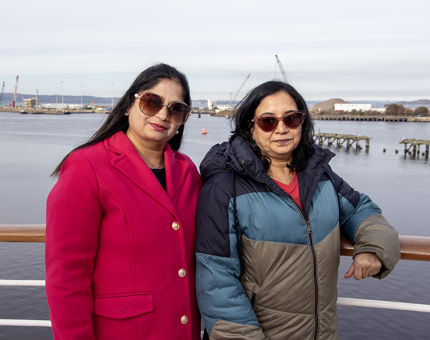 Two women wearing sunglasses stand on the Verandah Deck overlooking the water. 