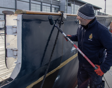 A man from the Maintenance team using a roller to paint The Royal Yacht Britannia's hull.