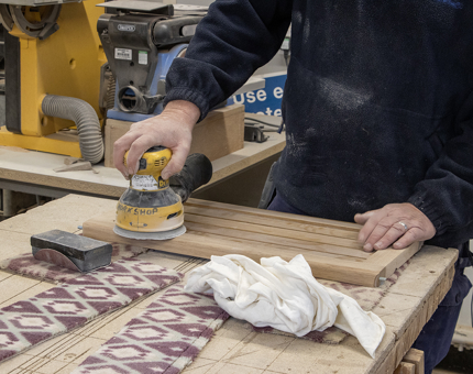 A member of the Maintenance team using a sander on wood to create a drinks trolley. 