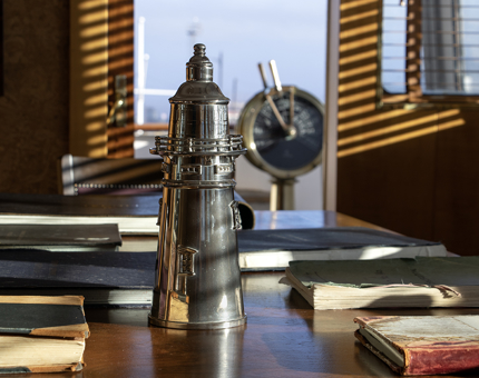 A lighthouse-shaped silver wine cooler with the ship's telegraph in the background at Fingal. 