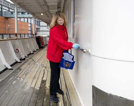 A Housekeeper cleans a railing on the Shelter Deck level at Britannia. 