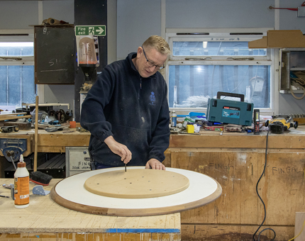 One of the Maintenance Team building a small round wooden table in the workshop.