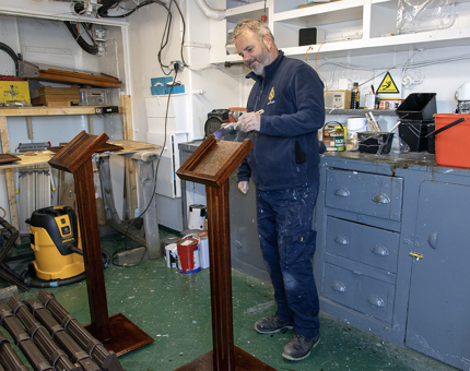 A man from the Maintenance Team varnishing wooden display plinths in the workshop. 