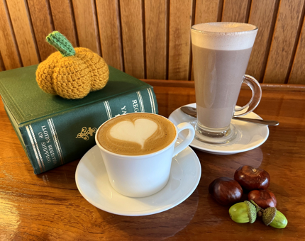 A pumpkin spice cappuccino, latte, book and crochet pumpkin. 