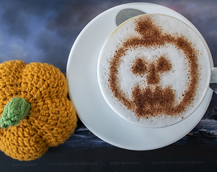 A decorative crochet pumpkin next to a pumpkin spice latte.