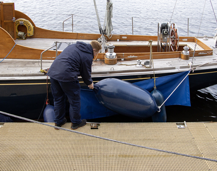 A member of the Maintenance Team attaches a fender onto the Royal Racing Yacht Bloodhound. 