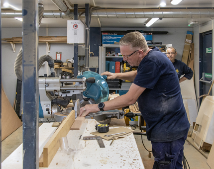 A man using a saw in the workshop to cut a length of wood. 