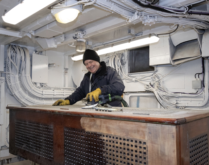 A member of the Maintenance Team sanding a rope box in the workshop.