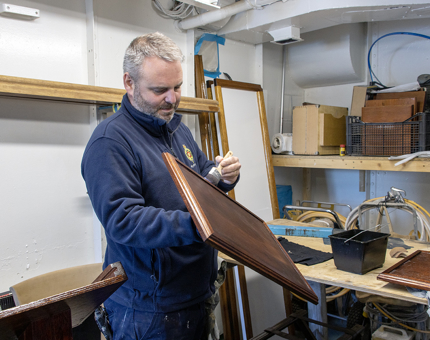 A man staining a wooden menu stand in the workshop.