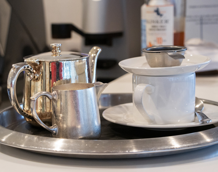 A tray with a silver pot of tea, saucer and cup as well as a milk jug.