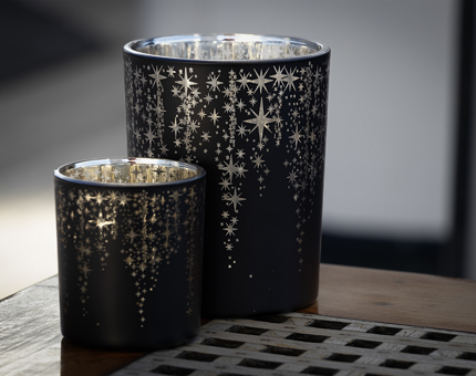 Two candles with star cut outs to allow light through the candle holder glass
