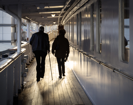 A couple walk along the Shelter Deck on Britannia as the sun sets. 