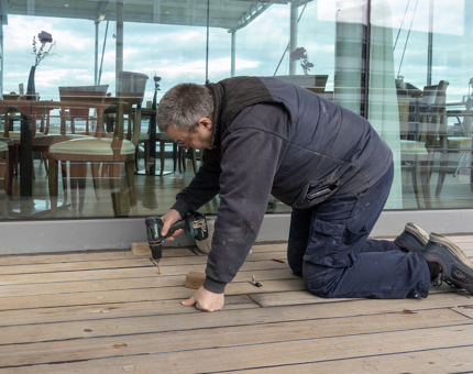 A member of the Maintenance team drilling into the wooden deck outside the Tearoom.