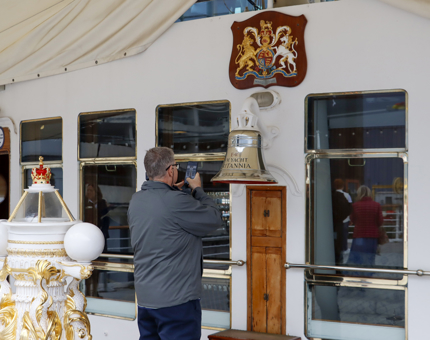 A man taking a photograph of Britannia's bell with his mobile phone on the Verandah Deck.