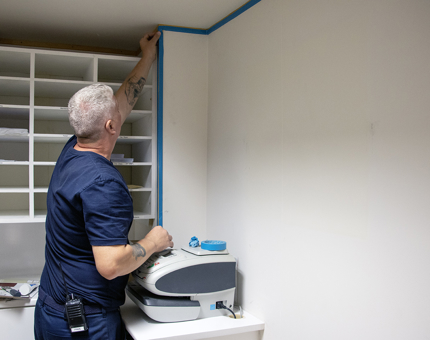 A man applying tape to the wall in the Visitor Experience office before painting. 