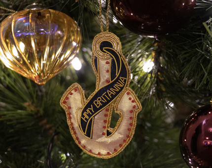 An embroidered Britannia hanging decoration in the shape of an anchor hangs on a Christmas tree. 