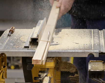 A closer view of the machine cutting the wood for the rope box seat pad base. 