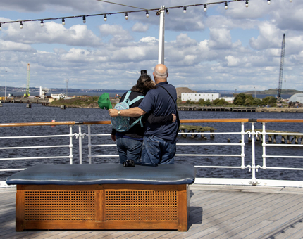 A couple stand on the Verandah Deck outside taking a selfie on a mobile phone. 