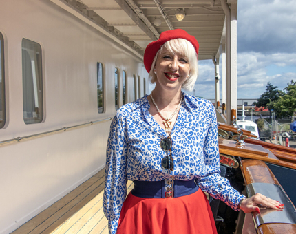 A woman wearing a bright red beret and skirt and blue shirt posing on the Shelter Deck. 