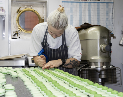 A pastry chef pipes filling into green macarons in the Galley. 
