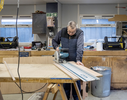 A man from the Maintenance team cutting wood in the workshop.