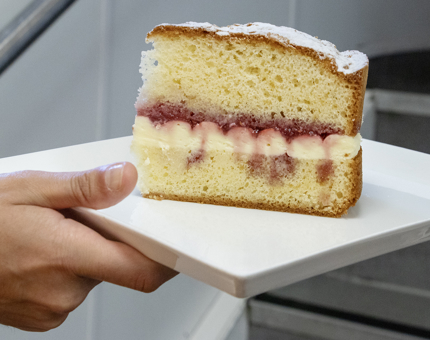A Waiter holding a plate containing a large slice of Victoria sandwich cake. 