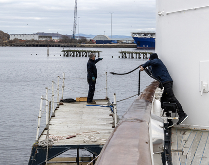 Two Maintenance men moving the floating platform. One is standing on the platform, and the other is throwing a rope to the man on the platform.