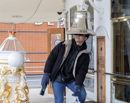 A man standing with his head inside the Bell on the Verandah Deck. 