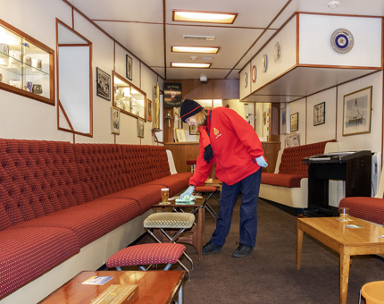A woman polishing a glass table in the Unwinding Room. There is a long bench that runs the length of the room and small tables and stools. 