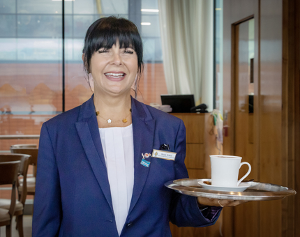 A member of the Tearoom team smiling and holding a tray containing  a hot drink in the Tearoom. 