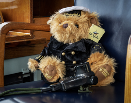 A fluffy teddy bear wearing a Captain's uniform and sitting in a chair. 