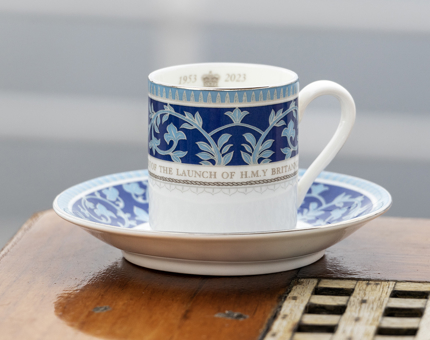 A blue and white espresso cup and saucer decorated with a celebratory design of the 70th anniversary of Britannia. 