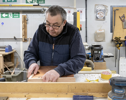 A man from the Maintenance team assembling a wooden frame in the workshop.