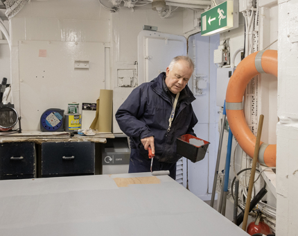 A member of the Maintenance team using a roller brush to paint the front panel for the Royal Barge pond filtration unit. 