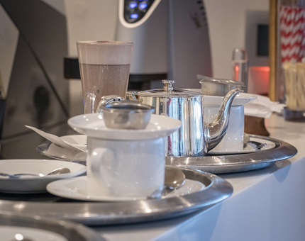 Two silver tea trays containing teapots, teacups and saucers.