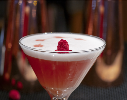 A red coloured-cocktail with a raspberry on top.