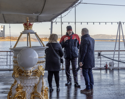 Man in red and blue coat talk to two people in black 