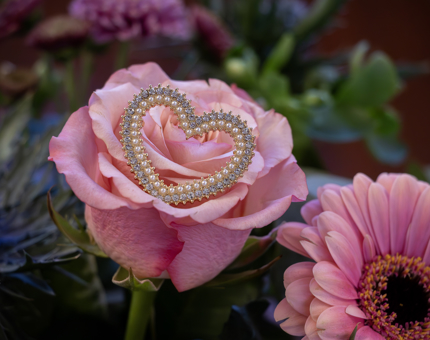 A diamante and pearl encrusted heart brooch displayed on a pink rose. 