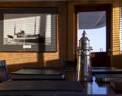 Morning sunlight casts shadows in Fingal's Bridge. A silver lighthouse-shaped wine cooler is on the table and a black and white photograph of Fingal is hanging on the wall.
