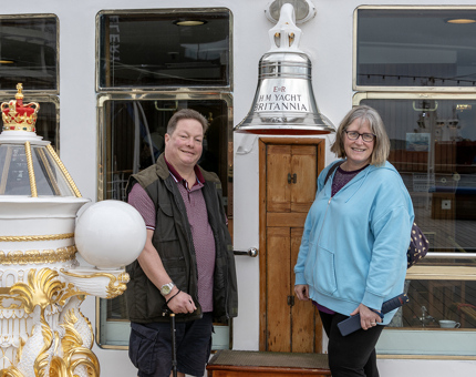 A man and a woman standing smiling either side of Britannia's Bell. 